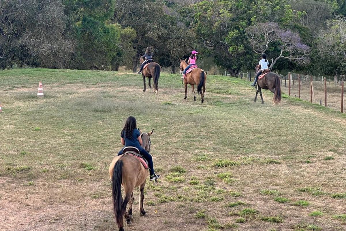 Quatro hóspedes cavalgando em fila pelo pasto da Villa Sinhá Ana, com a mata do cerrado ao fundo no fim da tarde.