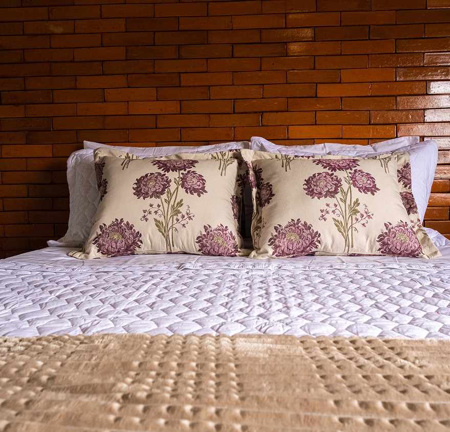 Cama queen arrumada em um dos chalés, junto à parede de tijolo aparente.