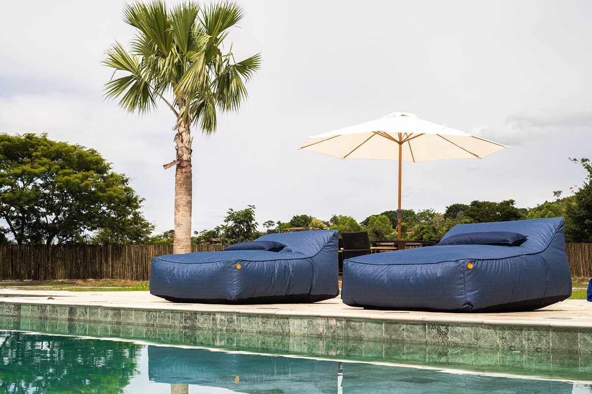 Espreguiçadeiras infláveis e guarda-sol branco na borda da piscina.