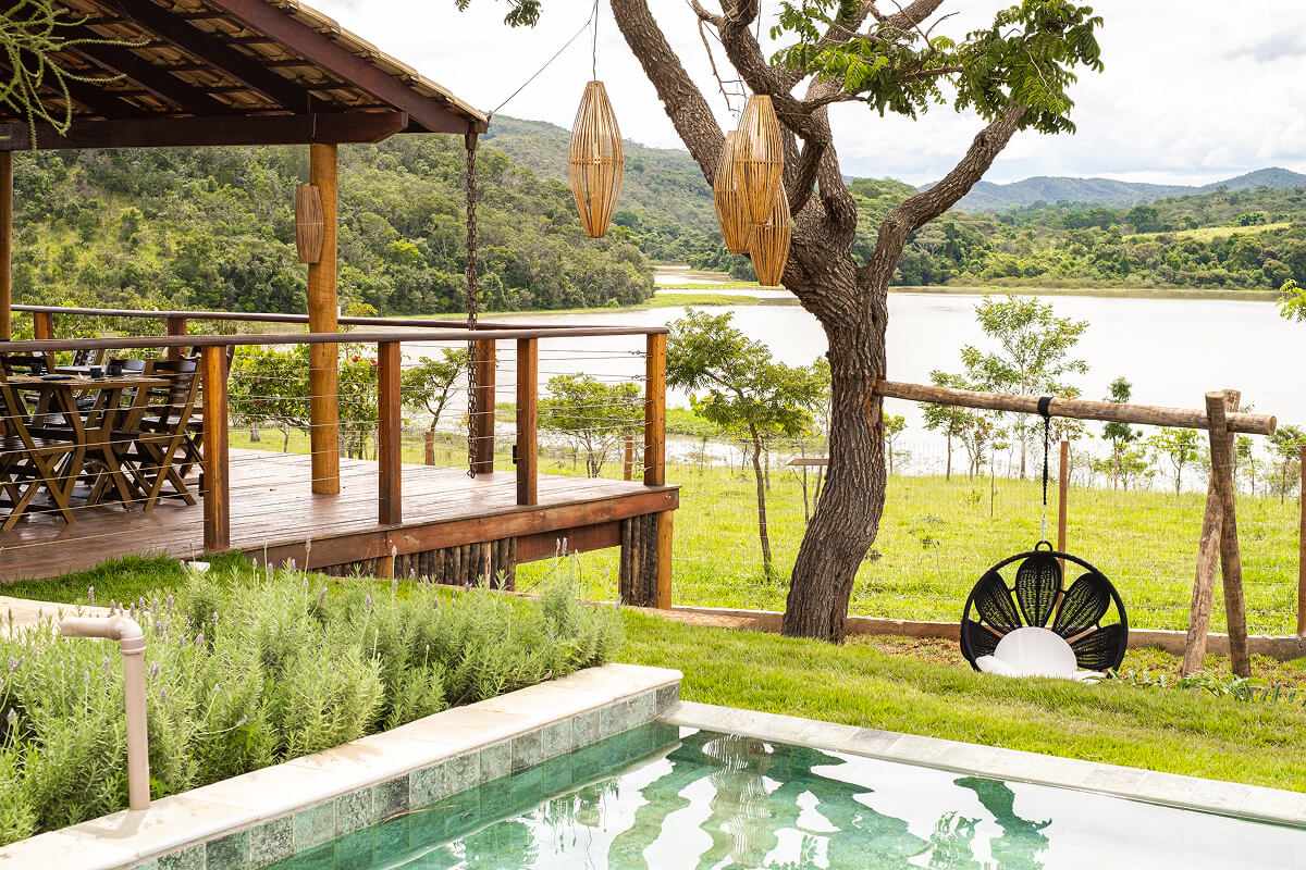 Deck de madeira coberto ao lado da piscina, com luminárias de bambu e o Lago Corumbá IV ao fundo.