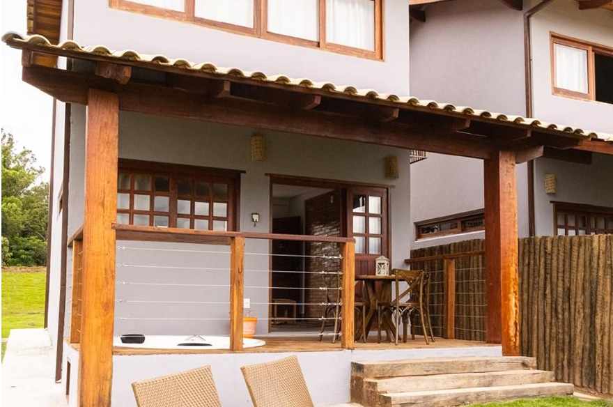 Varanda térrea do bangalô com pilares de madeira, telha cerâmica e jacuzzi embutida.