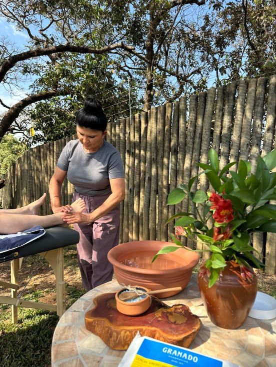 Profissional realizando uma massagem ao ar livre, sob as árvores, na Villa Sinhá Ana.