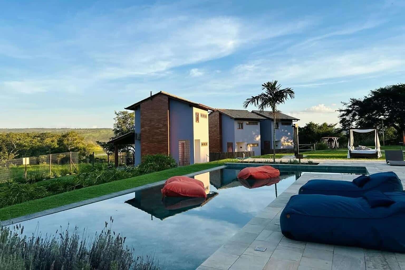 Piscina de borda espelhada refletindo o céu, com os bangalôs de tijolo ao fundo e o cerrado se abrindo até o horizonte no fim da tarde.